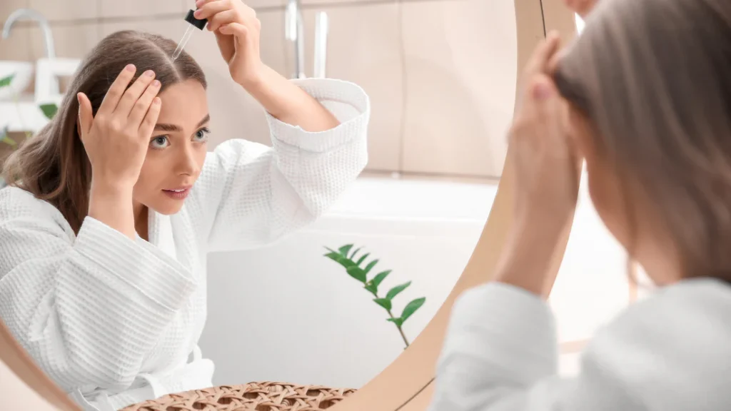 Woman applying minoxidil with a dropper to her hairline in front of a mirror