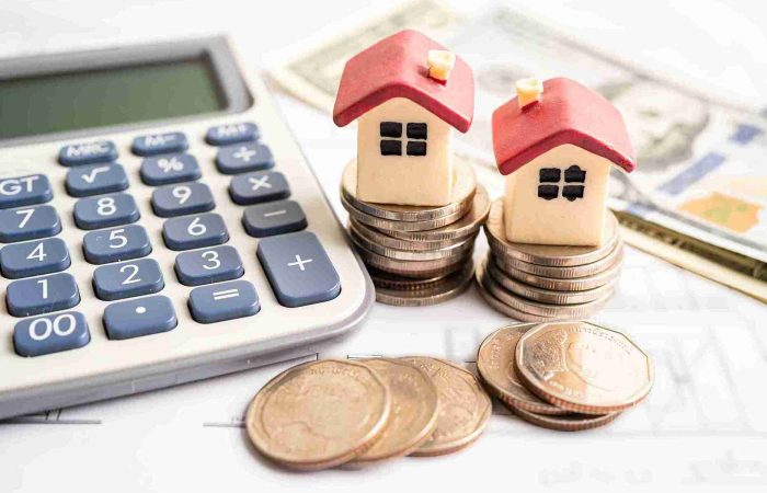 Haartransplantation Ratenzahlung – Schönheit auf Raten 6 Links liegt ein Taschenrechner, rechts daneben ein Haufen Geld und Münzen mit kleinen Häusern