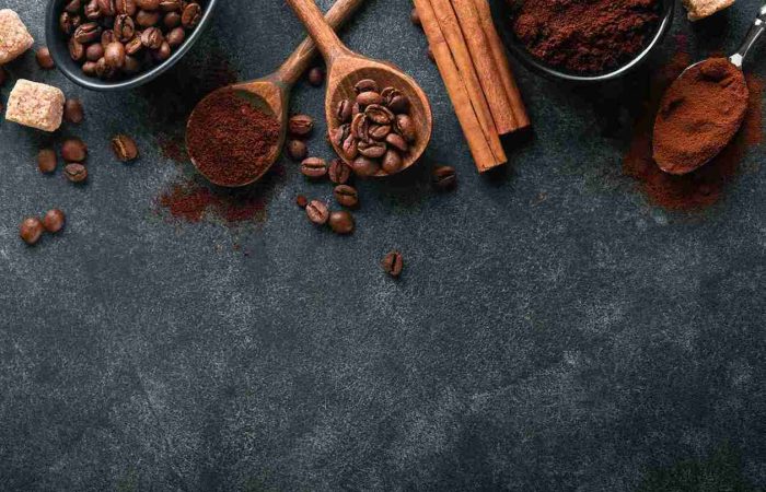 Kaffee nach Haartransplantation: Ist das gesund? 15 Kaffeebohnen, Kaffeepulver und Zimt auf dunkler Oberfläche – Symbolbild für Kaffee nach Haartransplantation und seine Wirkung.