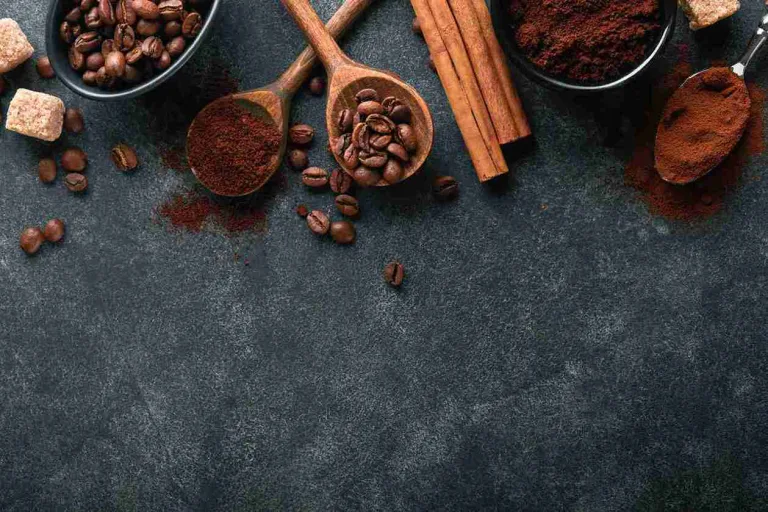 Kaffeebohnen, Kaffeepulver und Zimt auf dunkler Oberfläche – Symbolbild für Kaffee nach Haartransplantation und seine Wirkung.
