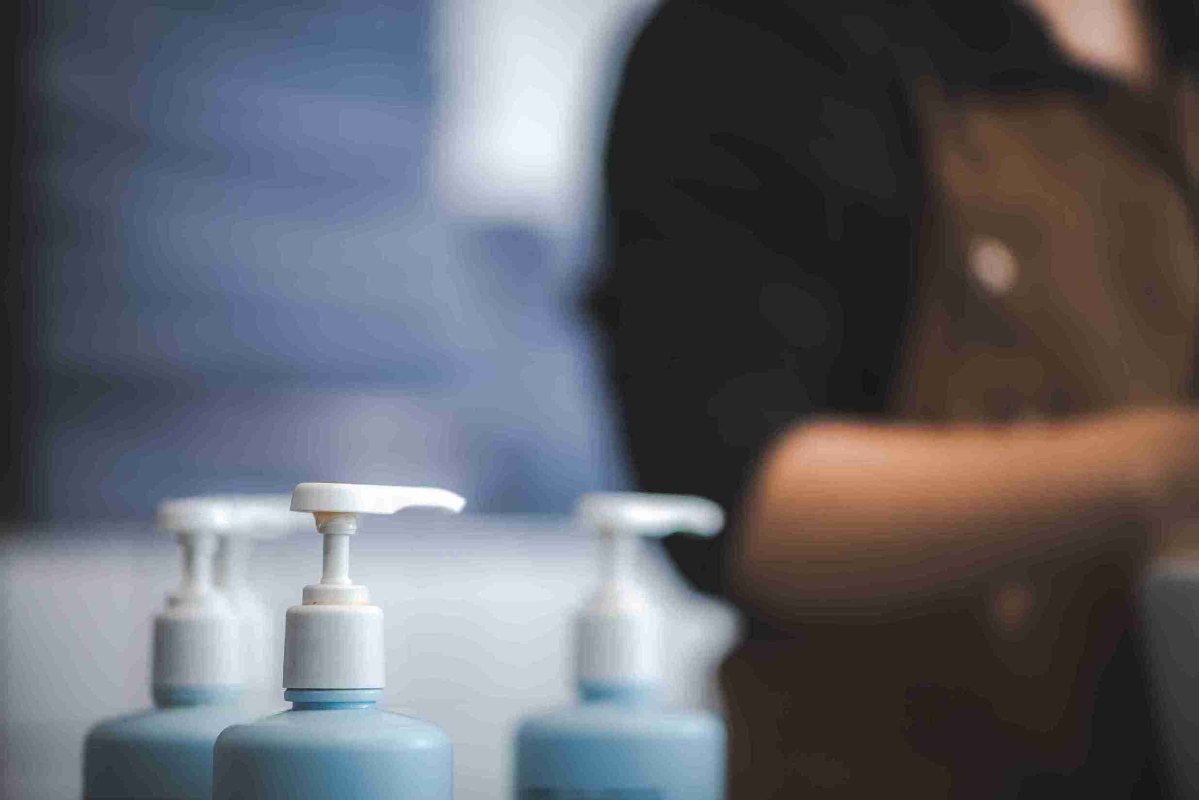 Mehrere blaue Spenderflaschen mit weißem Pumpverschluss, stehen für Shampoo nach Haartransplantation, in unscharfem Hintergrund einer Person in einem Salon oder einer Klinik.