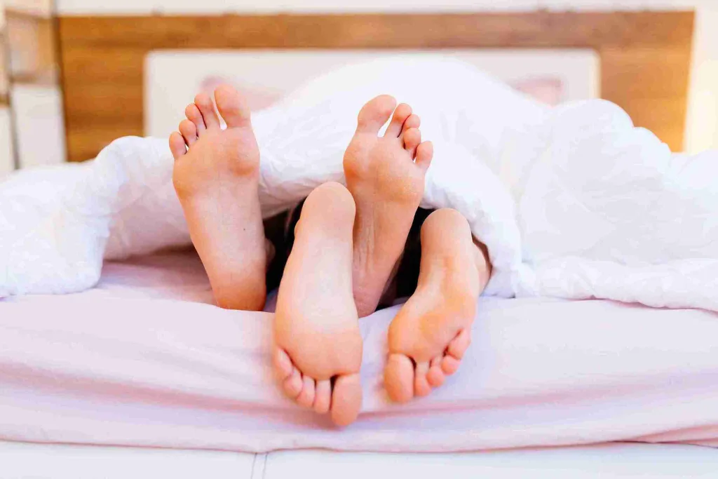 Symbolisches Bild für Sex nach Haartransplantation – zwei Personen liegen im Bett unter einer Decke, ihre Füße ragen hervor.
