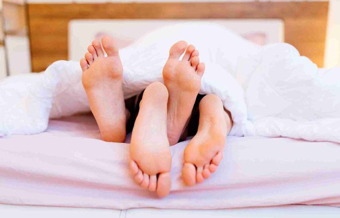 Sex nach Haartransplantation: Wann ist es wieder sicher? 5 Symbolisches Bild für Sex nach Haartransplantation – zwei Personen liegen im Bett unter einer Decke, ihre Füße ragen hervor.