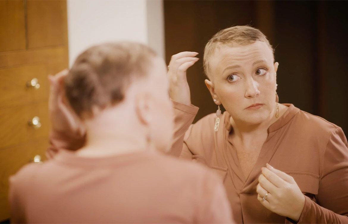 Woman with very short, thinning hair checking her hairline in the mirror, a sign of traction alopecia