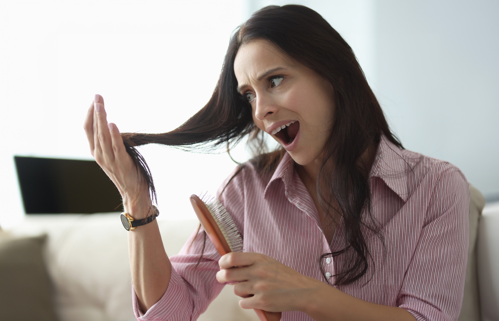 Seasonal Hair Loss: Causes, Recovery & Treatment Guide 4 Woman looking alarmed at loose strands of hair while holding a hairbrush