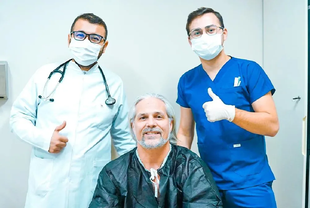 Paziente con i capelli lunghi e grigi con un medico e un membro del team con il pollice in su