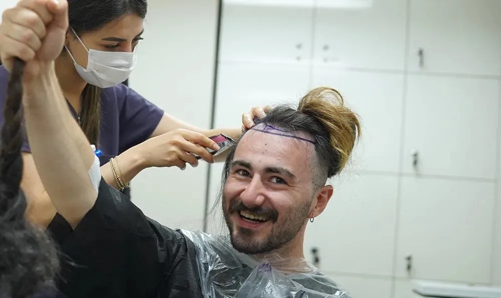 Membro del team che taglia i capelli lunghi di un paziente sorridente prima di un trapianto FUE a capelli lunghi