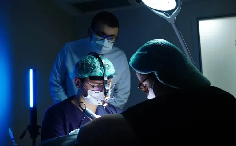Team chirurgico intorno a un paziente in una sala operatoria illuminata di blu, con un medico che supervisiona