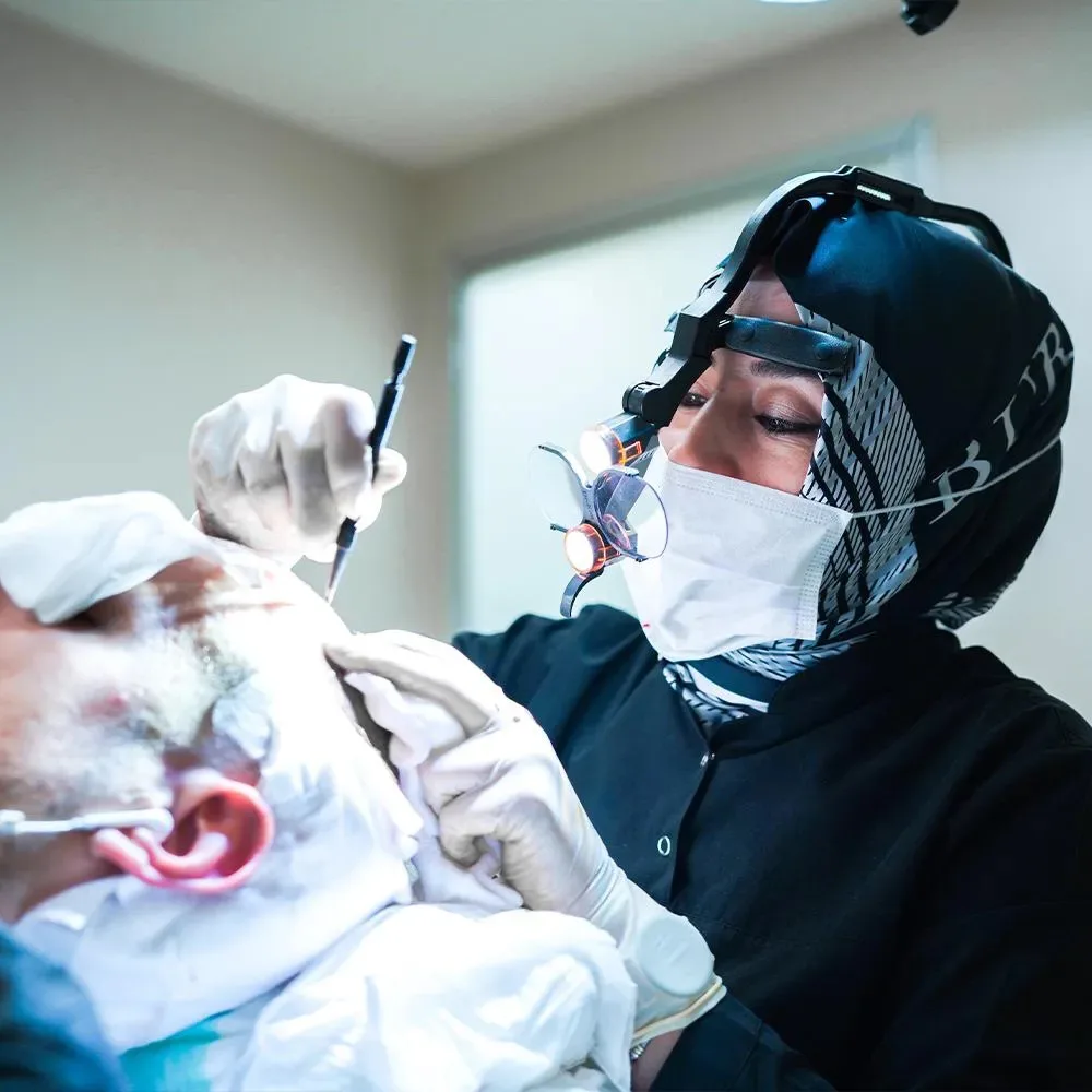 Chirurgienne en foulard avec loupes implantant des greffons sur un patient allongé