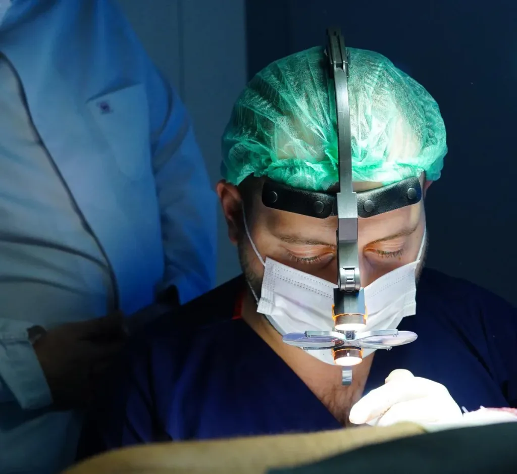 Chirurgien en charlotte avec lampe frontale et loupes, concentré sur un patient