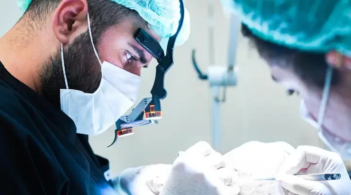 Chirurgien avec loupes travaillant avec concentration sur le cuir chevelu d'un patient