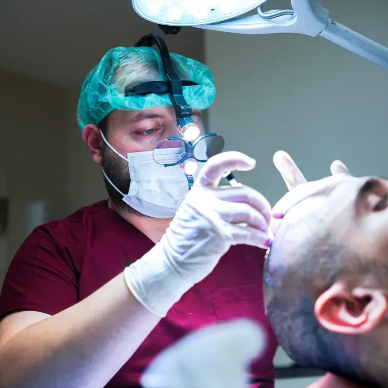Chirurg mit Stirnlampe und Lupenbrille untersucht die rasierte Haarlinie eines Patienten