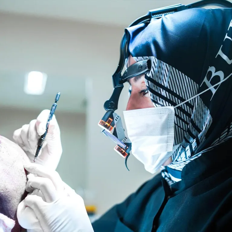Chirurgin mit Kopftuch und Lupenbrille arbeitet an der Haarlinie eines Patienten