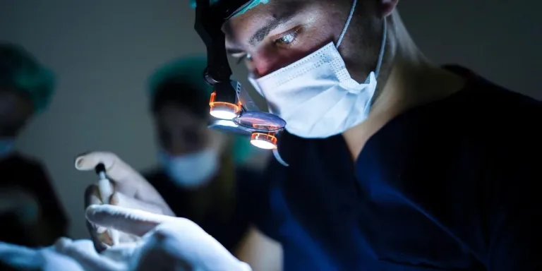 Chirurgien avec loupes et lampe frontale tenant un instrument dans une salle d'opération sombre
