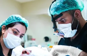 Chirurgo con lenti d'ingrandimento e assistente che trattano un paziente