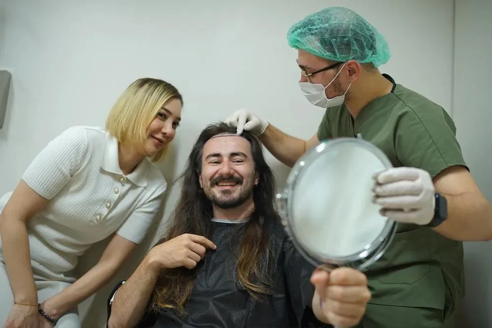 Paziente sorridente con i capelli lunghi accanto a una donna e a un medico che tiene uno specchio a mano